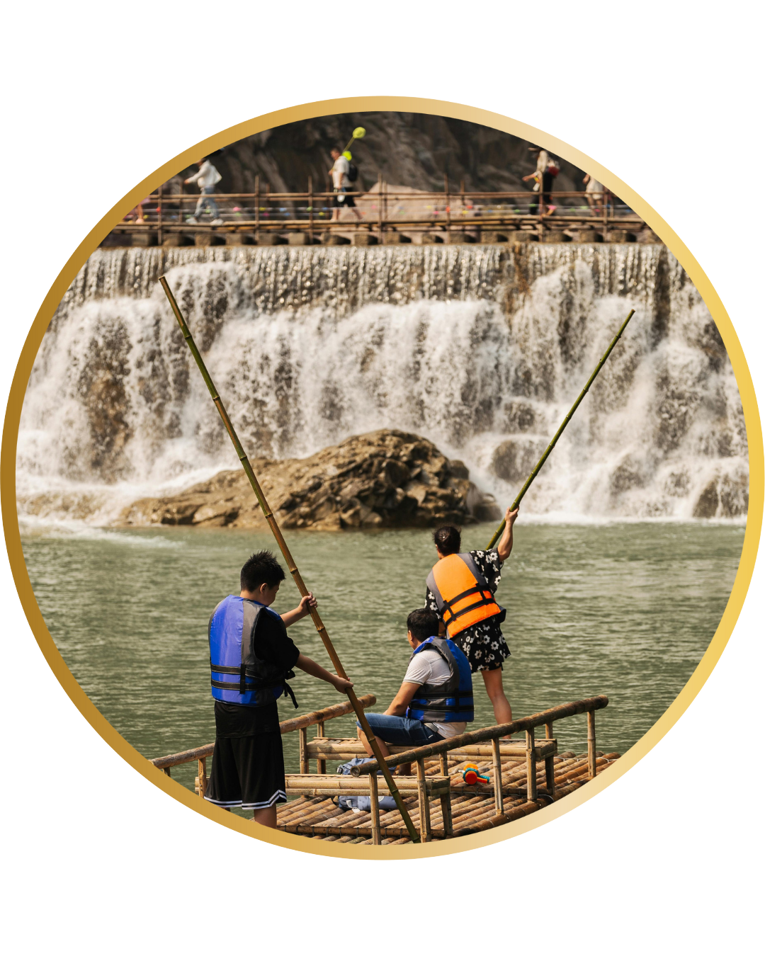 Three people in life vests stand on a bamboo raft with long poles on a river. A waterfall flows in the background, while people are seen on a bridge above, all part of an exciting India Tour Package by Dravin Group